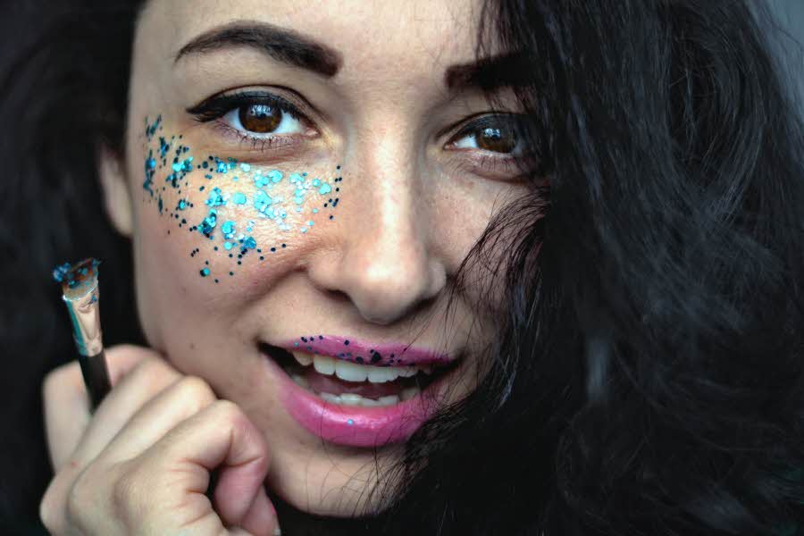 Jente holder sminkekost og har dekorativ blå glittersminke under øyet
