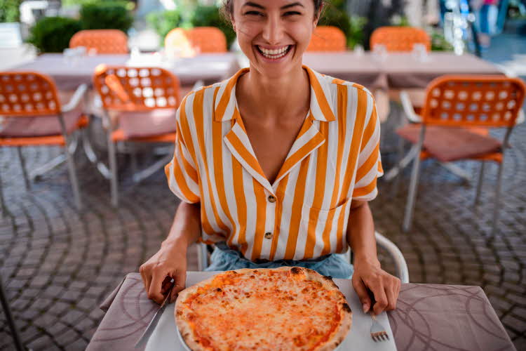 Smilende jente i stripede oransje skjorte matcher pizza og stolene