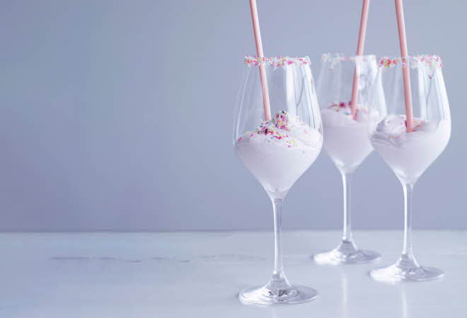 Tre vinglass med rosa kremet drikk og fargerike strøssel.