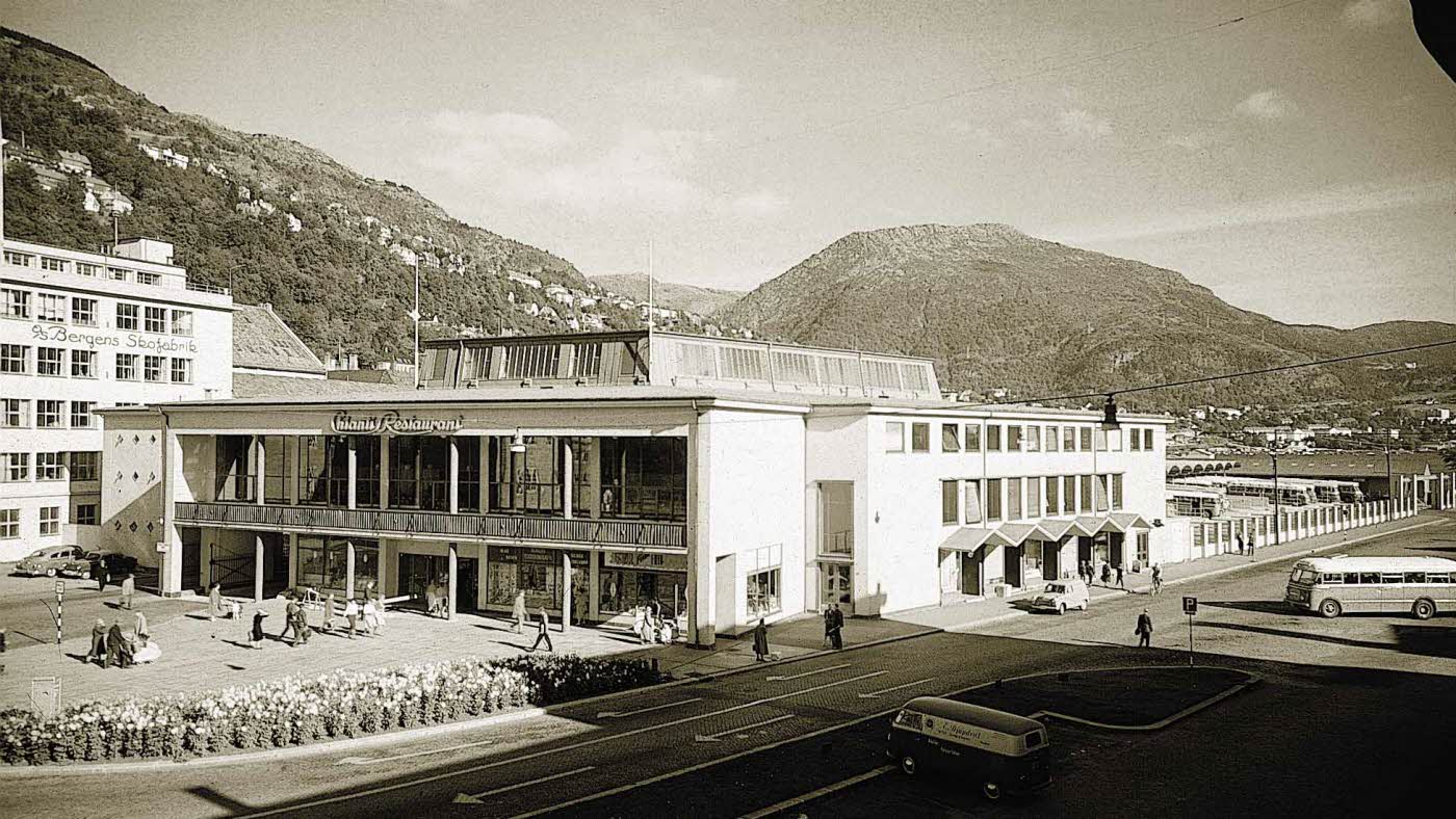 Svart-hvitt bilde av arbeider med en bygning foran fjell
