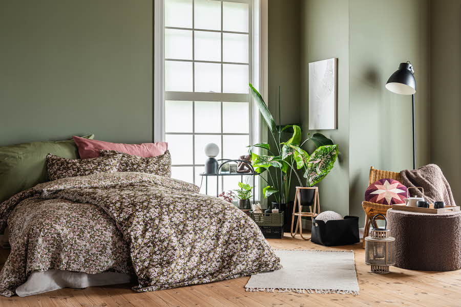 En seng med mønstret sengesett, grønn og rosa pute.