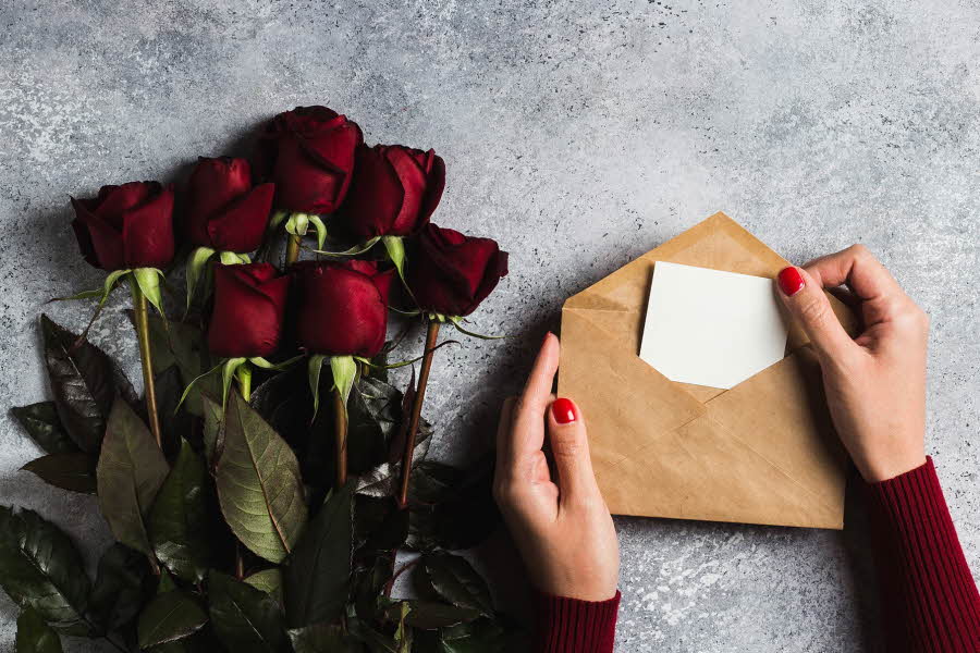 Dame åpner konvolutt ved siden av en bukett med roser