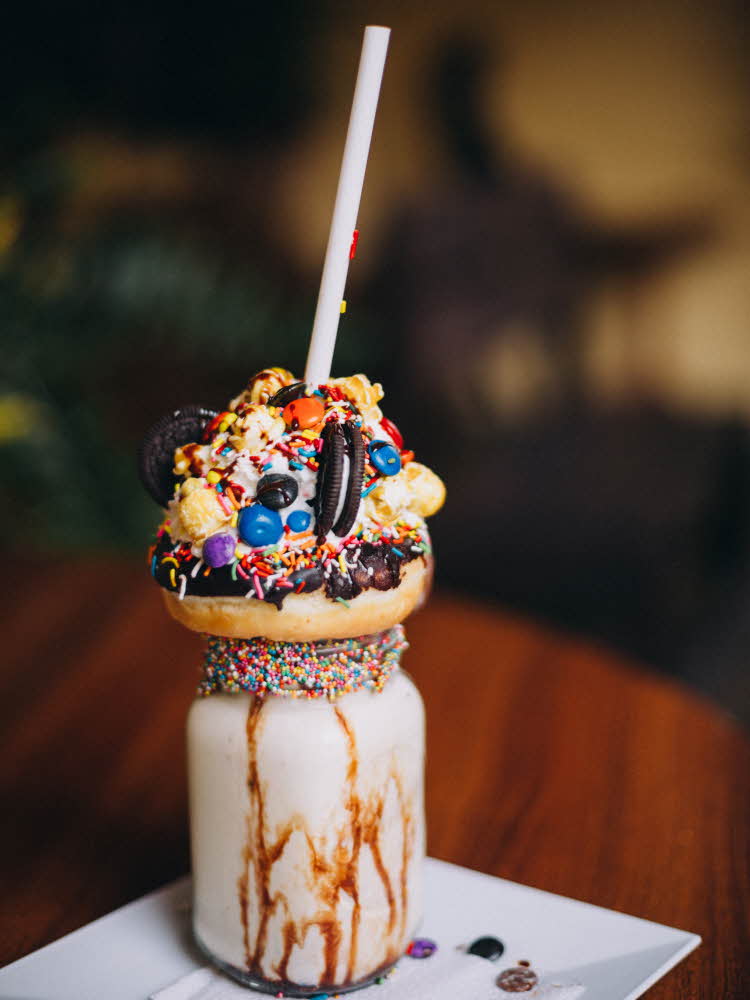 Syltetøyglass med milkshake oppi, donut oppå pyntet med kjeks og med sugerør oppi. Kan minne om en tåteflaske. Illustrasjonsfoto til artikkel om kaker til babyshower.