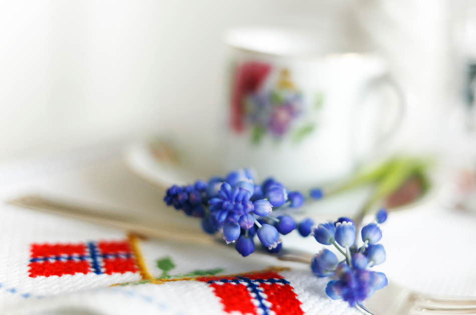 Blå perleblomster på et bord med duk med broderier av det norske flagget. Foto til artikkel om borddekking til 17. mai