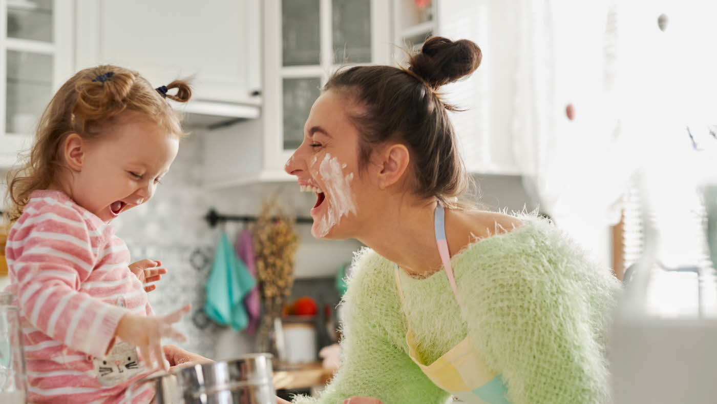 Mor og datter som smiler og ler mens de baker på kjøkkenet