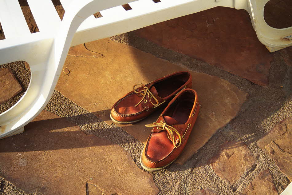 Nærbilde av brune seilersko med lærlisser stående på steingrunn under hvit solstol i plast