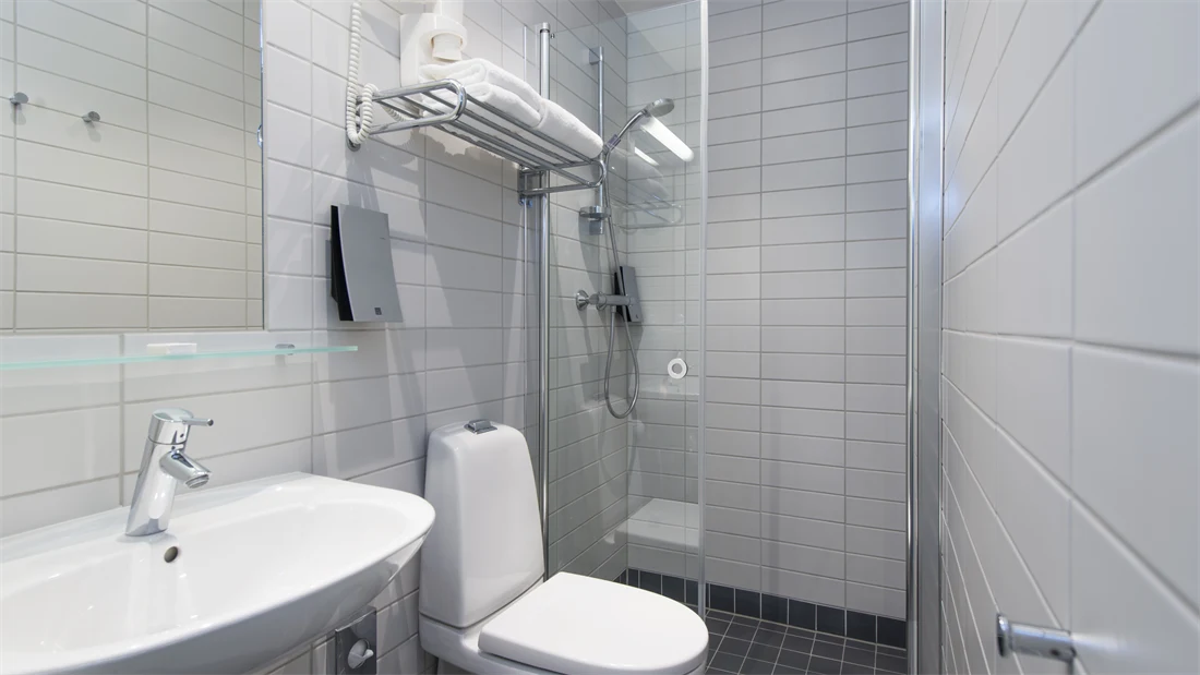 Standard bad på Thon Hotel Trondheim. Hvit innredning. Grå fliser på gulvet. Badet inneholder dusj, servant, speil og toalett.