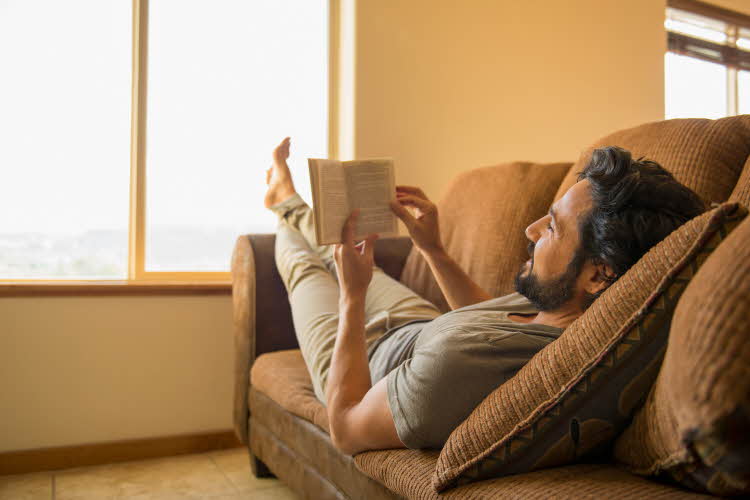 avslappet mann som ligger i sofa og leser en bok