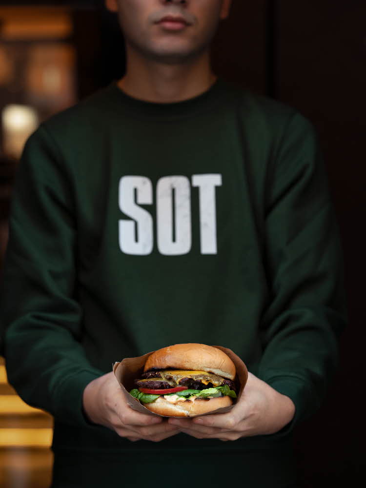 gutt med grønn genser som holder en hamburger