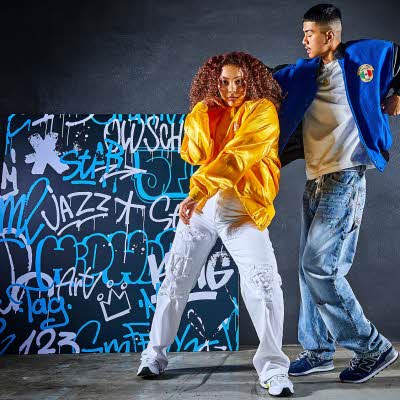 to ungdommer i trendy klær som danser foran en vegg med graffiti