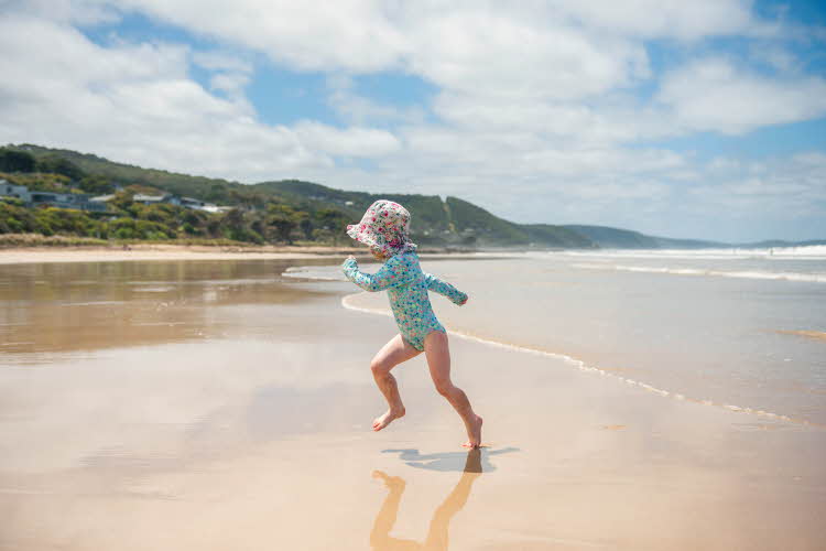Barn løper på strand med uv-drakt og solhatt