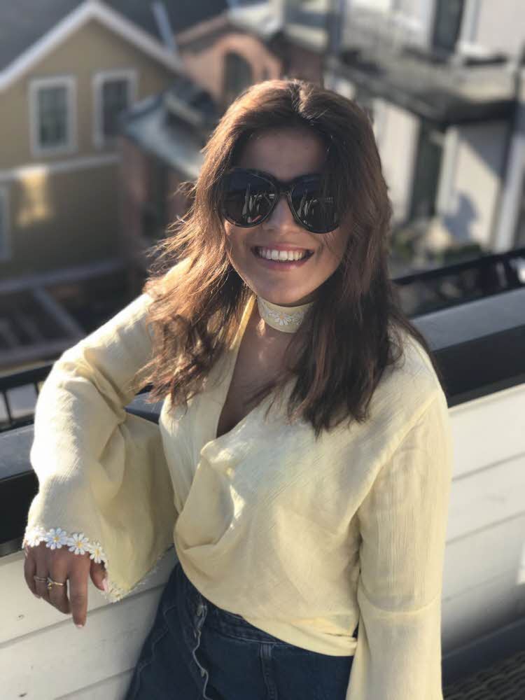 Brunette smiler til kamera iført gul topp og kort dongeriskjørt