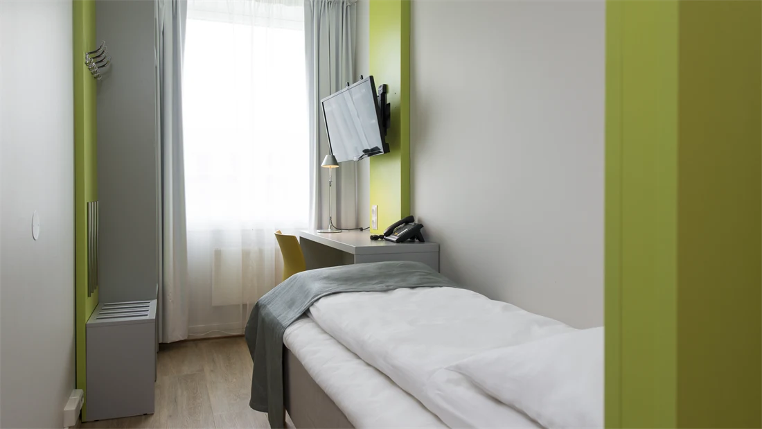 Small Single Room på Thon Hotel Trondheim. Hvite vegger med innslag av grønne flater. Oppredd seng, TV og lite skrivebord.