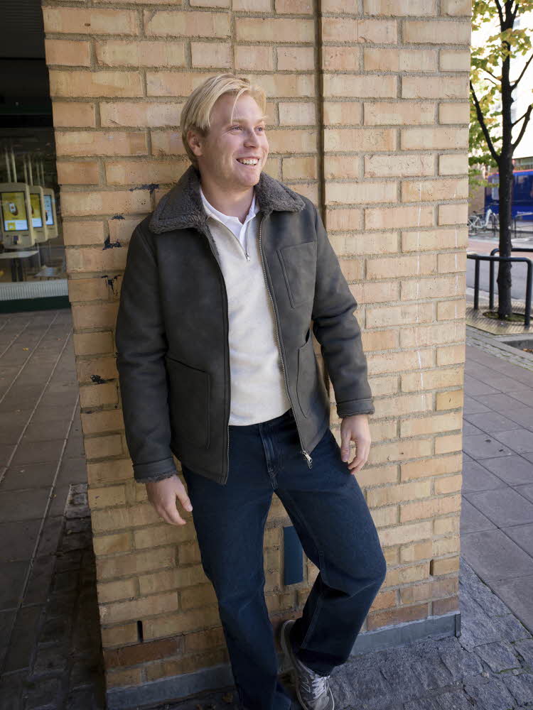 Gutt i grå jakke, hvit genser og hvit t-skjorte, jeans og sneakers.