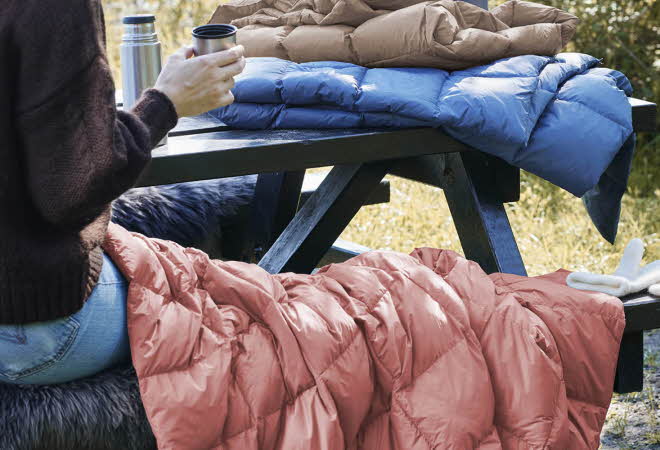 En kvinne som sitter på et bord ute med et Hygge dunpledd over beina sine.