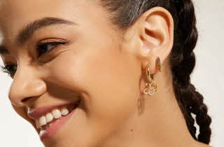Et nærbilde av en kvinne som smiler ut til siden, hun har to øreringer i gull i øret