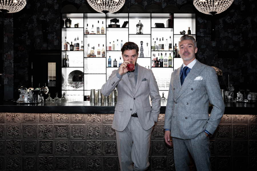 To menn i grå dress står i en bar.
