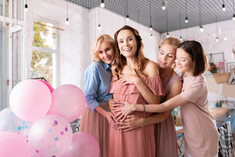 babyshower med damer som står rundt gravid dame omringet av rosa ballonger