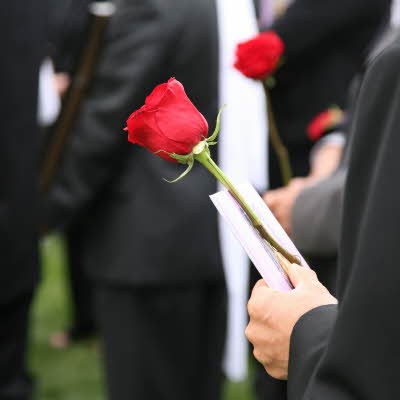 Person i sort dress holder en rød rose blant andre dresskledde mennesker i en begravelse
