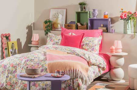 En seng med rosa og blomstrete sengesett på seg