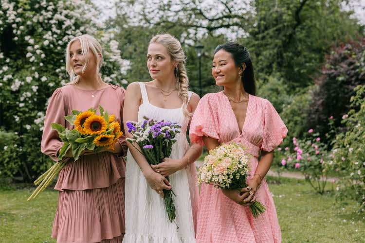 Tre damer i kjole som holder blomsterbuketter