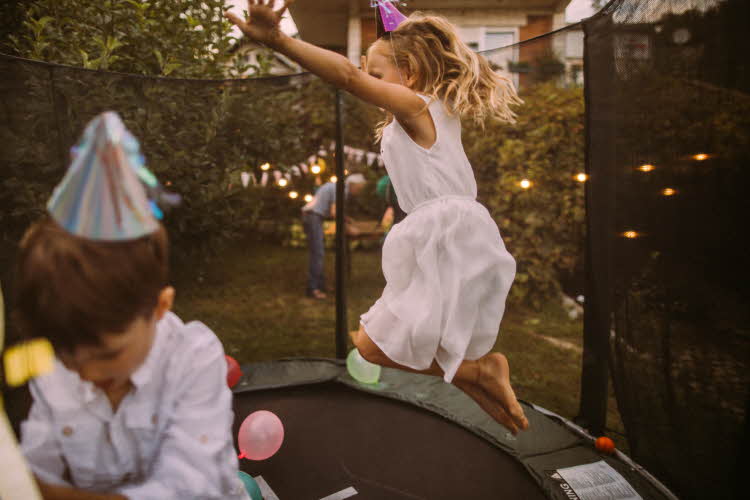 Jente og gutt med bursdagshatt hopper på trampoline fylt med ballonger