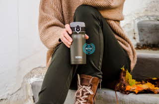 En person som sitter på en trapp ute med en termoskopp i hånden.