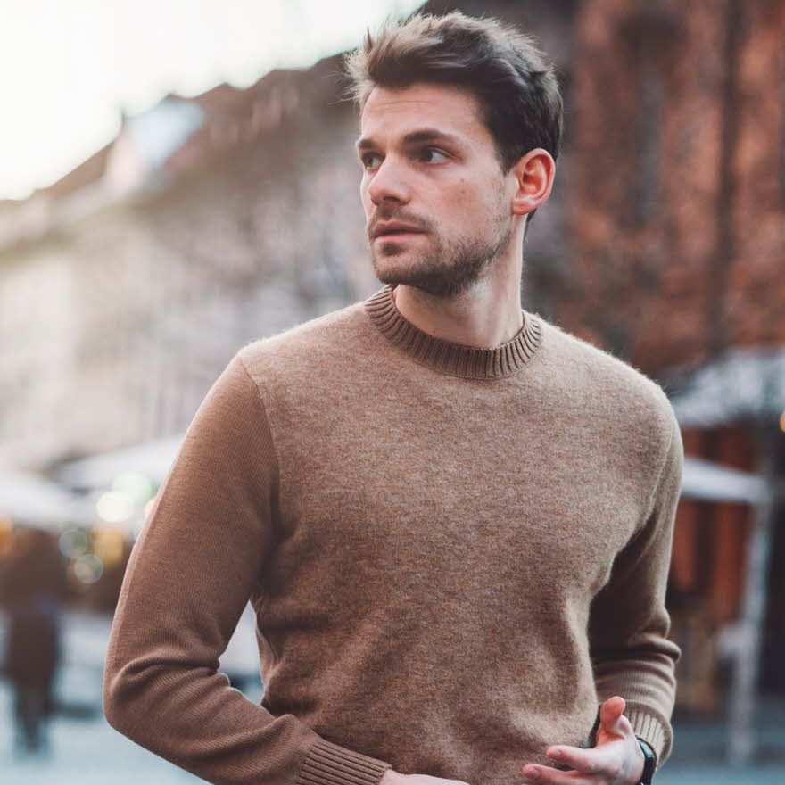 Mann i brun ullgenser poserer foran kamera utendørs på vinterlig gate 