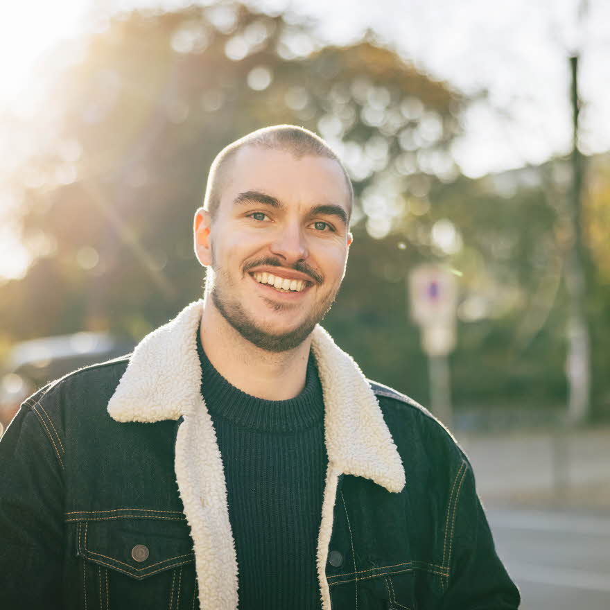 Mann med foret olajakke med pelskrage smiler utendørs 