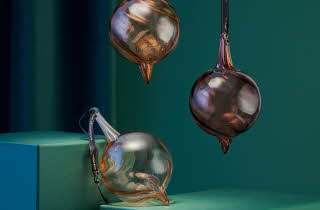 Tre Champagneklang julekuler fra Hadeland Glassverk, to som henger og en som ligger støttet opp.