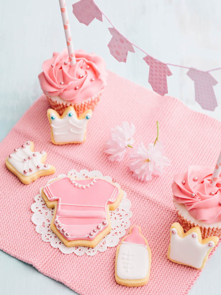 Kjeks og muffins dekorert med babytema i rosa. Illustrasjonsfoto til artikkel om kaker til babyshower..