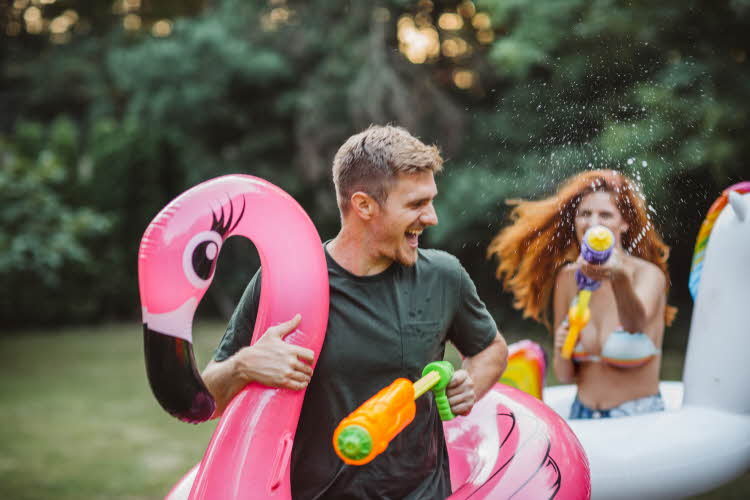 Vannkrig i hage med mann som løper med rosa flamingo som blir sprutet vann på av dame bak