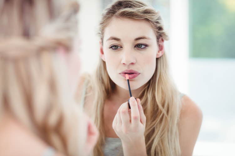 Kvinne tar på lipgloss i speilet på badet.