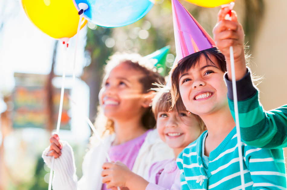 Tre barn som smiler med ballonger i hendene