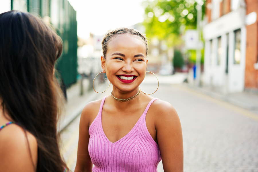 Smilende jente i knallrosa topp, øreringer og rød leppestift står i en gate.