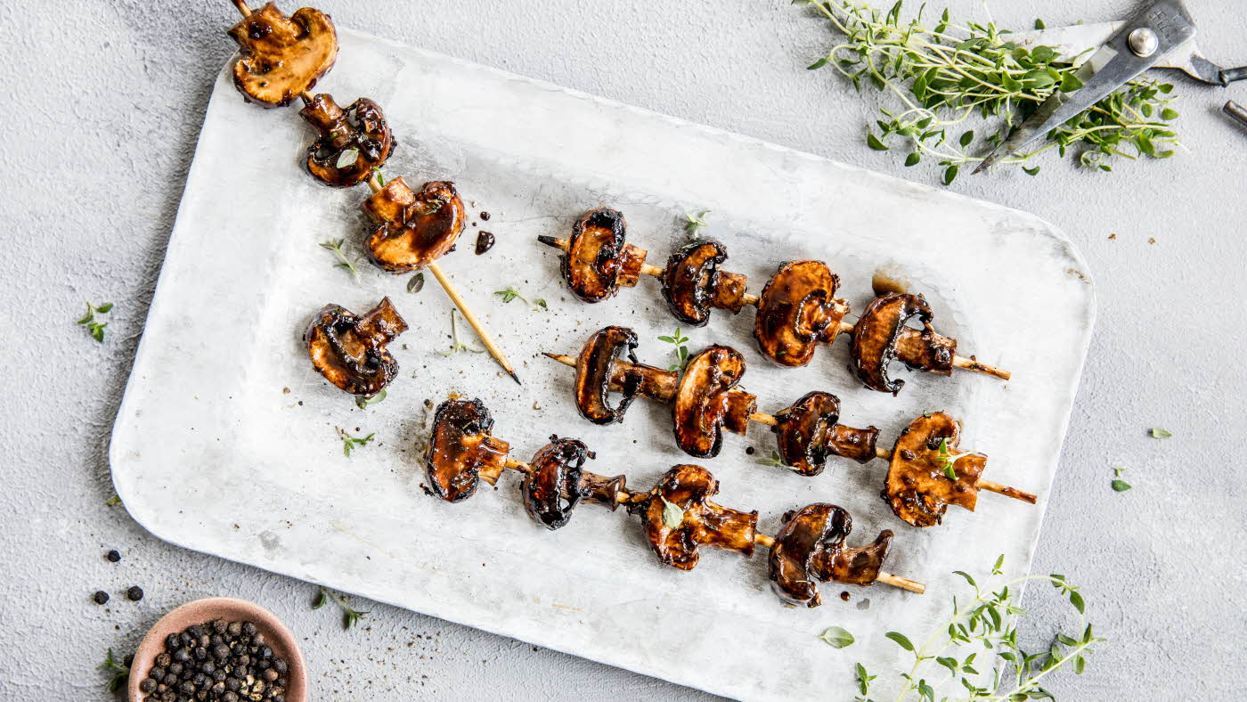 Grillspyd med grillet sopp på hvitt fat med urter rundt