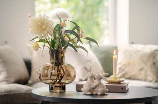 Rundt bord med vase med blomster, tent lys og keramiske kaninfigurer.