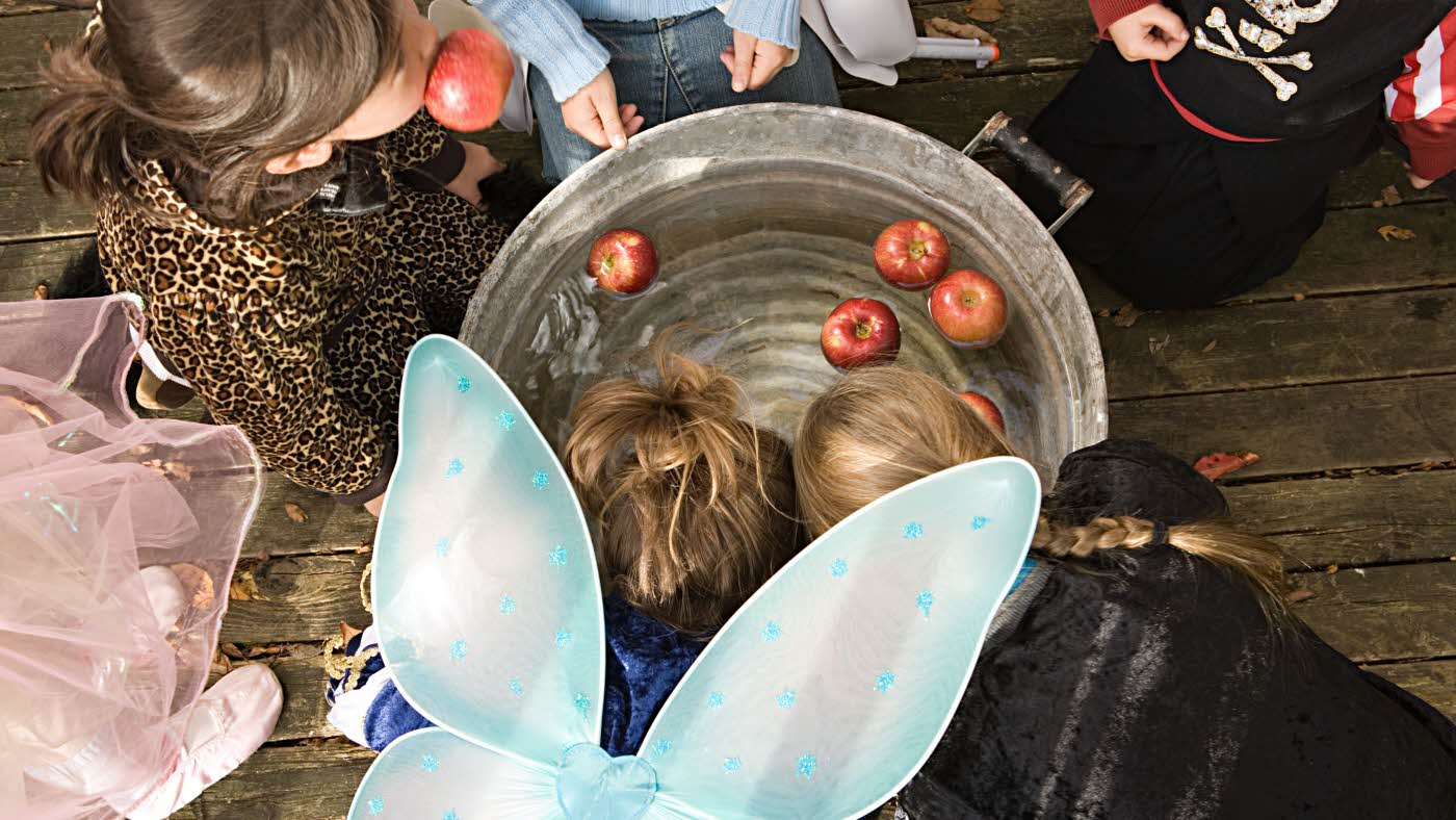 Barn biter i eple som ligger i stålbøtte med vann utkledd til halloween