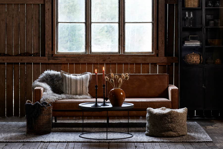 En fin innredet sofakrok med puter, pledd og lys på bordet.