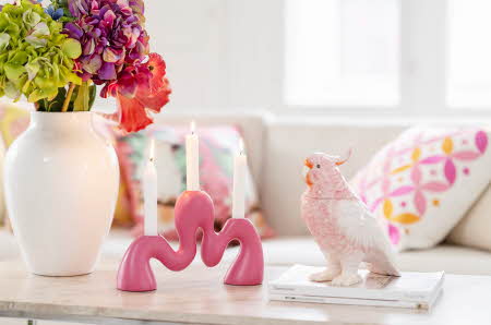 Et borde med en vase med blomster, en rosa lysestake og en figur av en rosa fugl