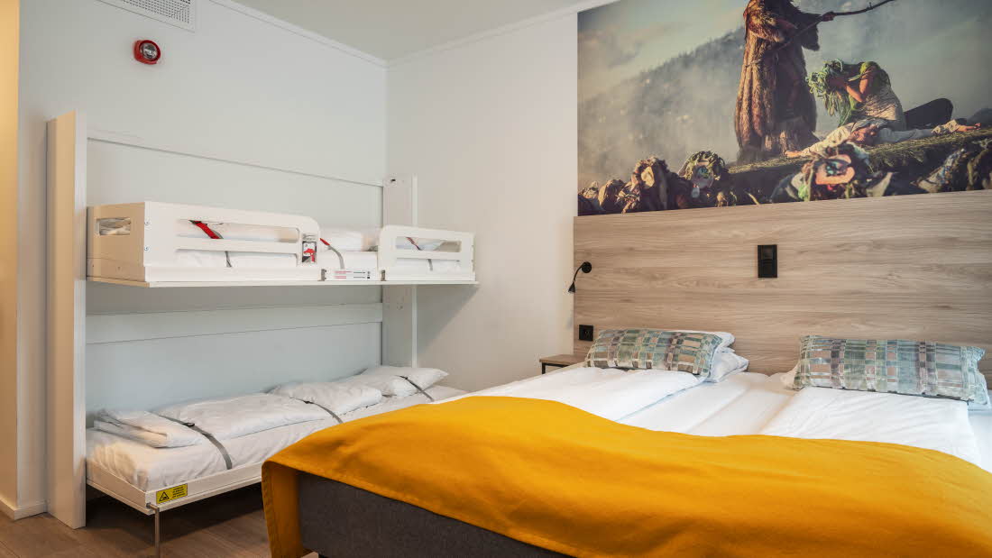 Chambre familiale avec lits superposés et un lit double. Au dessus de la tête de lit est accroché un tableau représentant Peer Gynt.