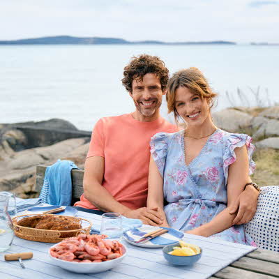 En mann og en kvinne sitter ved et bord ute ved vannet med reker på bordet