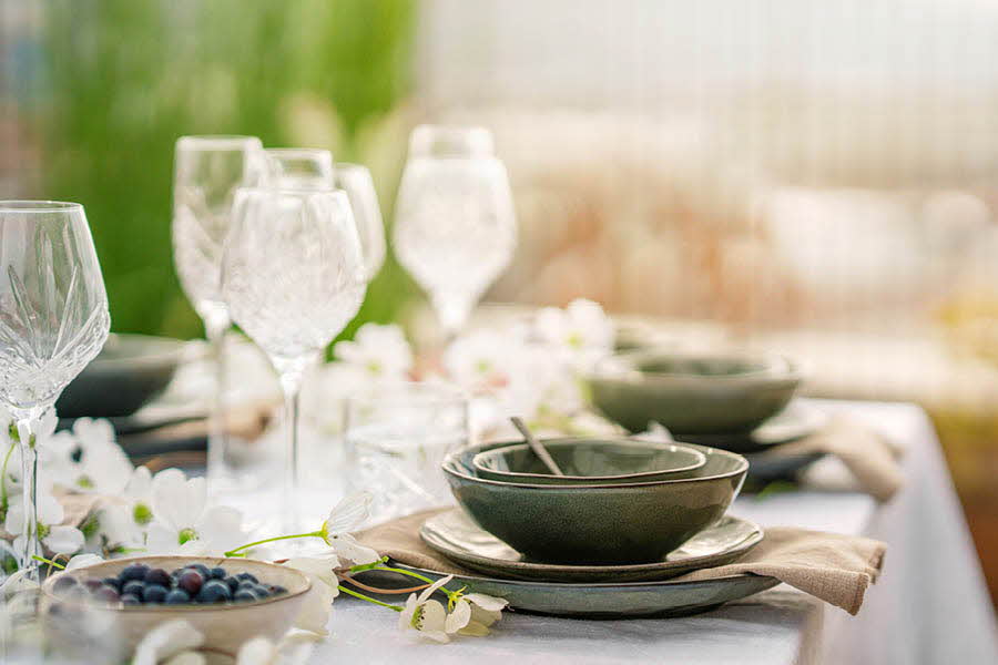 Grønne tallerkener og skåler oppå et bord med hvit duk. Hvite blomster som dekor på bordet sammen med vinglass.