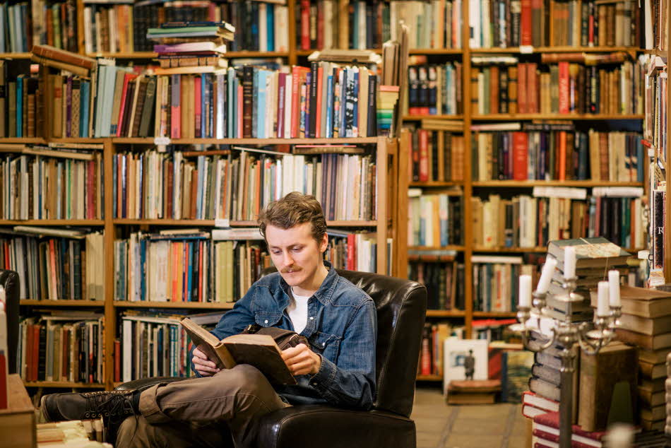 Mann sitter i lenestol og leser, bokhylle i uskarp bakgrunn. Foto til artikkel om julegave far blir glad for