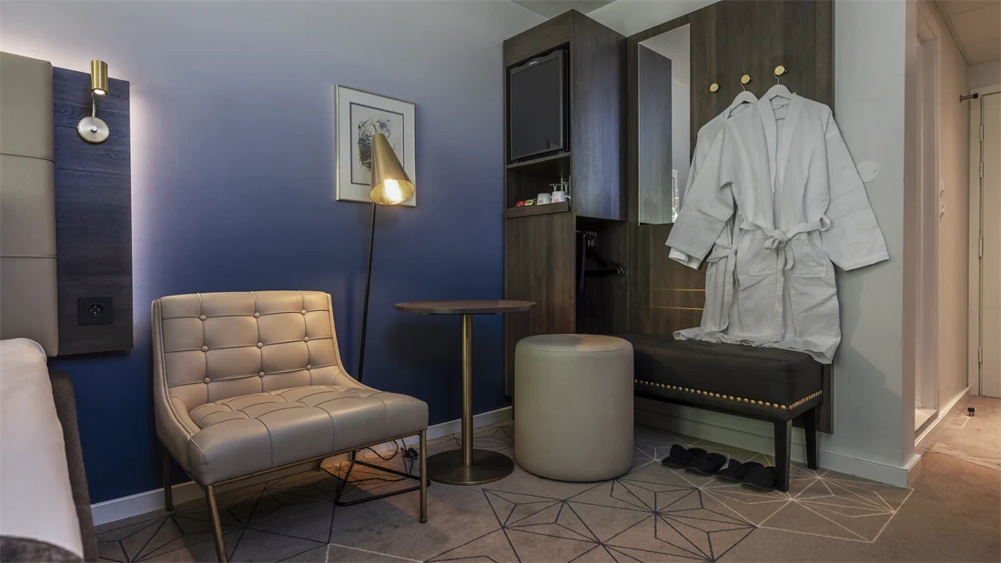 Superior rom med diverse møbler. Lenestol, lite bord, puff, stålampe, minibar og to morgenkåper som henger på veggen