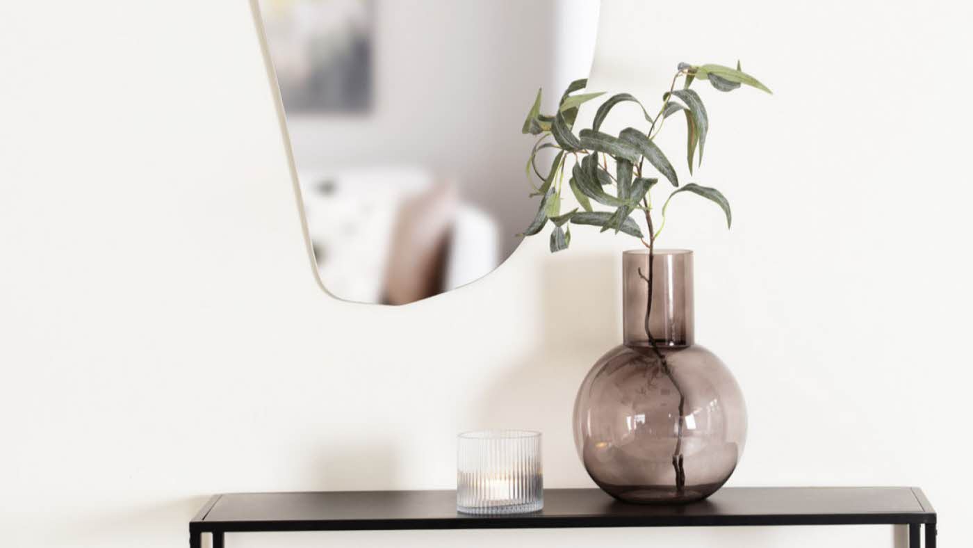 Vase står på konsollbord og det henger et ovalt speil på veggen