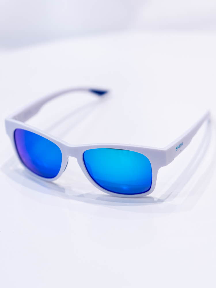 Brune solbriller som ligger på et hvitt bord med lysebrune brilleglass Hvite solbriller som ligger på et hvitt bord med knall blå glass fra Smith