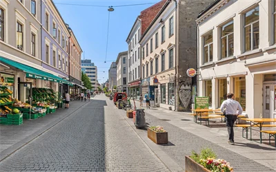 Handlegaten Torggata, sett fra øst til vest. Gågaten er pyntet med blomsterkasser og brostein. En grønnsakshandel på venstre side og restauranter med uteservering på høyre side.