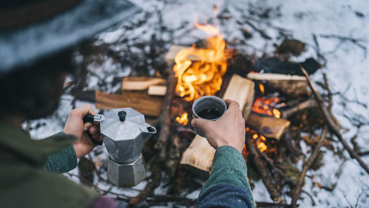 Bål i snø og mann som holder mokkakanne og kopp