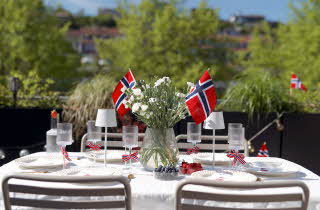 Bord dekket til utendørs måltid med norske flagg og to hvite utelamper.